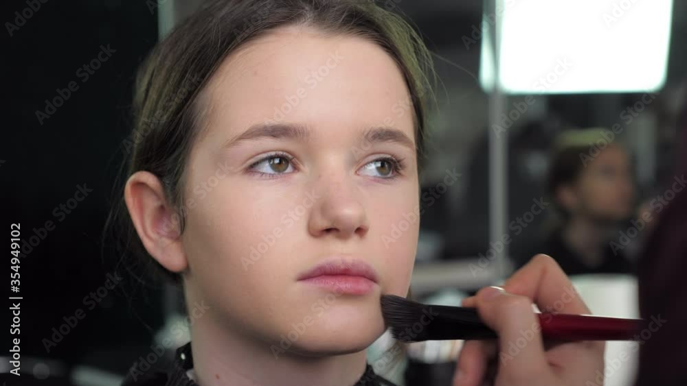Professional make-up artist applies foundation on her face with brush to a teenager girl in a beauty salon. 4K slow motion footage Professional make-up artist applies foundation on her face with brush to a teenager girl in a beauty salon. 4K slow motion footage
