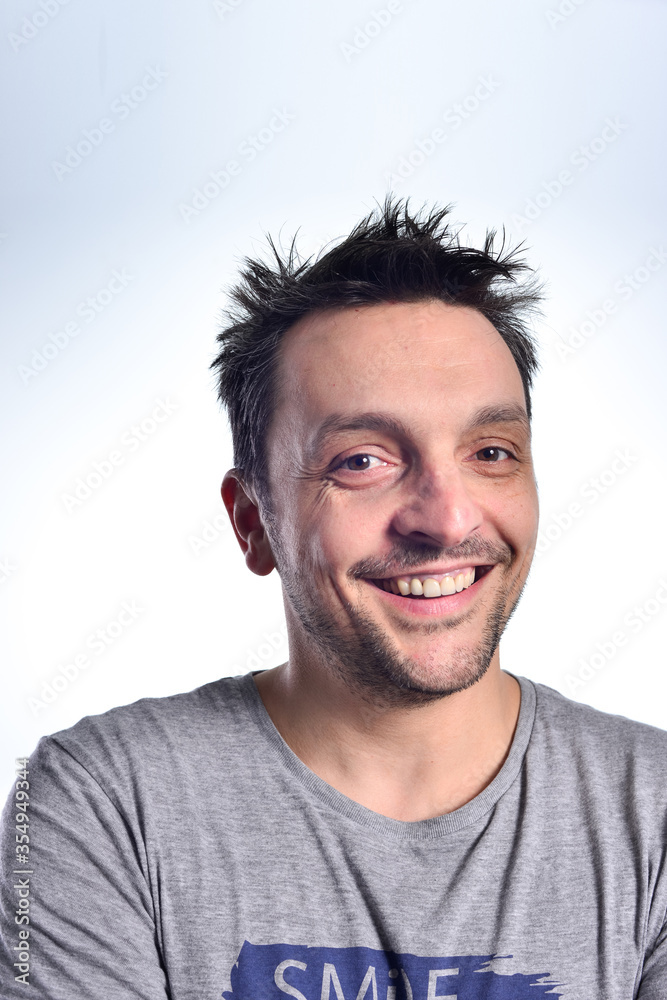 Young man dressed casual, sitting on a white chair, doing face expressions, isolated in white.