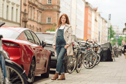 Beautiful young pregnant woman wearing casual clothes walking through the city streets. concept of motherhood and pregnancy. street portrait among cars close up view. © lialia699