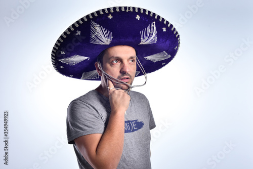 Young caucasian man dressed casual, wearing a mexican sombrero, doing face expressions, isolated in white.