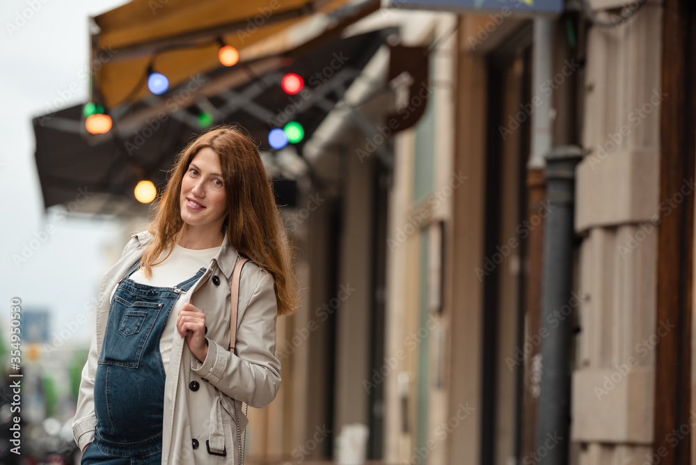 Fototapeta premium Beautiful young pregnant woman wearing casual clothes walking through the city streets. concept of motherhood and pregnancy. street portrait among cars close up view.