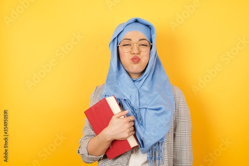 Beautiful young muslim woman wearing hijab puffing cheeks with funny face. Mouth inflated with air, crazy expression. © Jihan