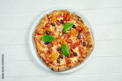 Appetizing, homemade pizza with margarita with cherry tomatoes, basil and mozzarella on a white plate on a white wooden background