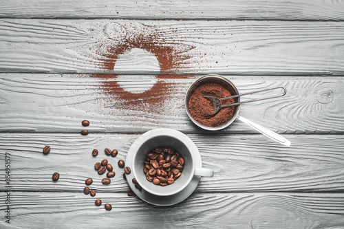 Cup and scoop with coffee beans and powder on wooden background
