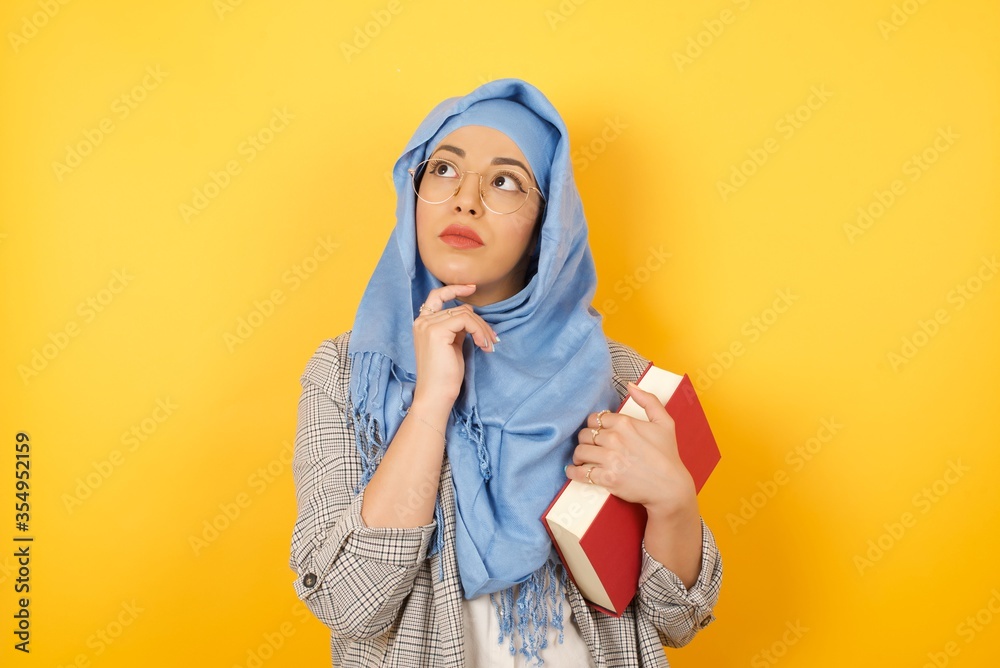 Face expressions and emotions. Thoughtful young muslim woman wearing hijab holding hand under her head, having doubtful look. Face expressions and emotions. Thoughtful young muslim woman wearing hijab holding hand under her head, having doubtful look.