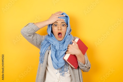 Horrible, stress, shock. Portrait of young emotional crazy young muslim woman wearing hijab clasping head in hands. Human emotions, facial expression concept. Trendy colors. Front view © Jihan