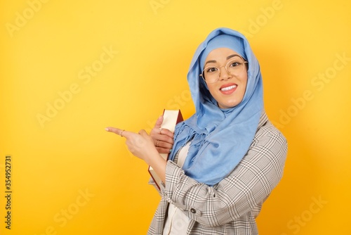 Positive attractive young muslim woman wearing hijab, points aside with cheerful and surprised expression with mouth opened, shows something amazing. Advertisement concept.