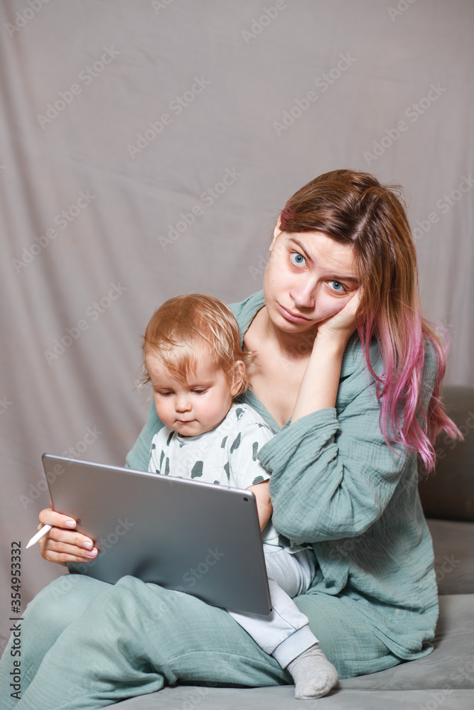 A young woman works at home with a tablet computer, along with a child.the son wants to communicate with his mother, they make noise and interfere with work.isolation during the coronovirus pandemic A young woman works at home with a tablet computer, along with a child.the son wants to communicate with his mother, they make noise and interfere with work.isolation during the coronovirus pandemic