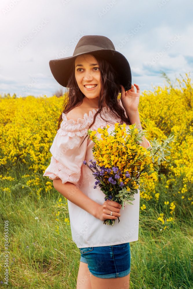 Photo of a beautiful woman in a black hat with a bouquet of wildflowers. Girl in a field of flowers with a bouquet.