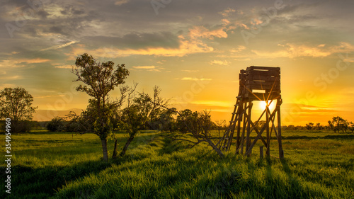 Ein Hochsitz auf einer Wiese vor einem dramatischem Sonnenuntergang