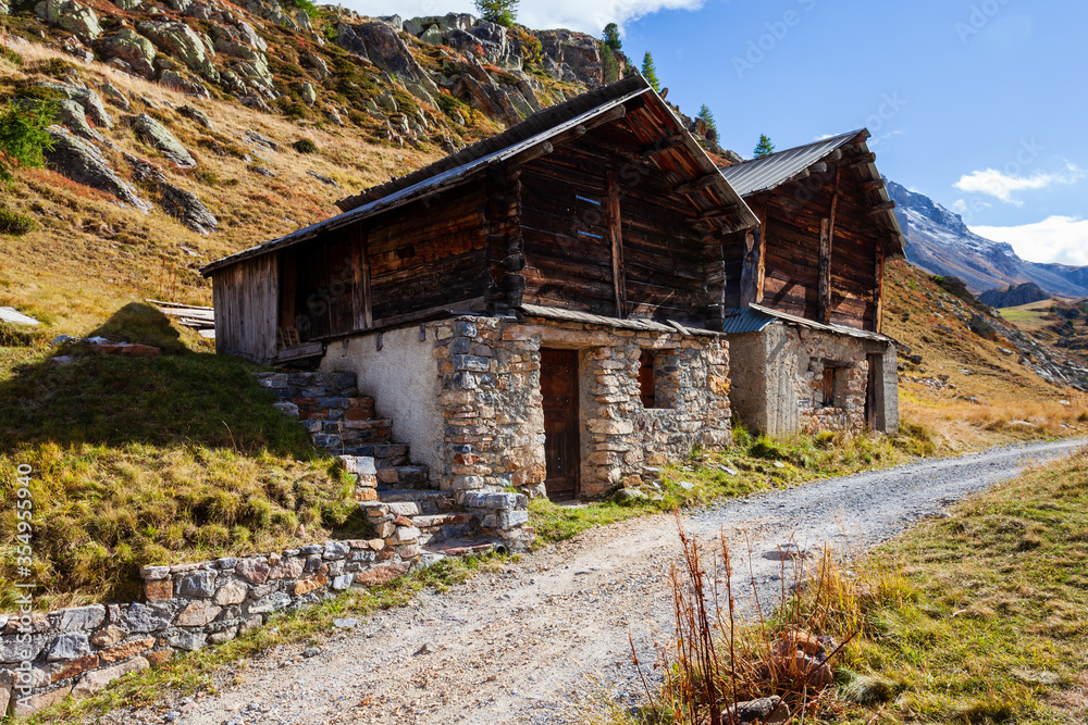 Wooden and stone made huts in Alps Mountains. Houses next to path dirt road. Alpine rural rustic architecture, Arvieux, France, Europe. Wooden and stone made huts in Alps Mountains. Houses next to path dirt road. Alpine rural rustic architecture, Arvieux, France, Europe.