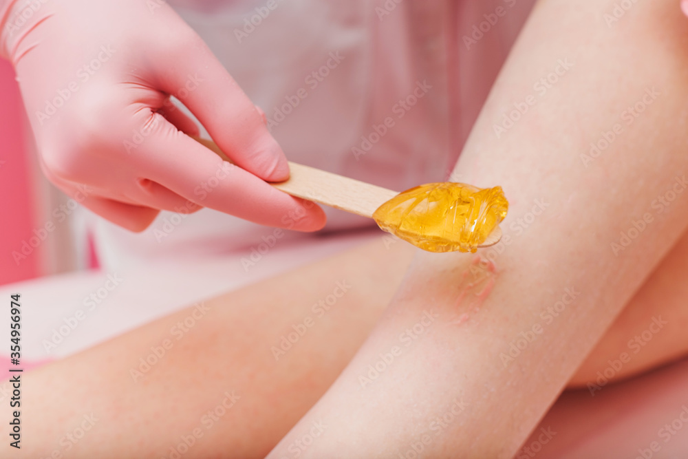 Sugaring. Young woman gets the procedure for hair removal liquid sugar. Beautician depilating young woman's legs with liquid sugar in spa center