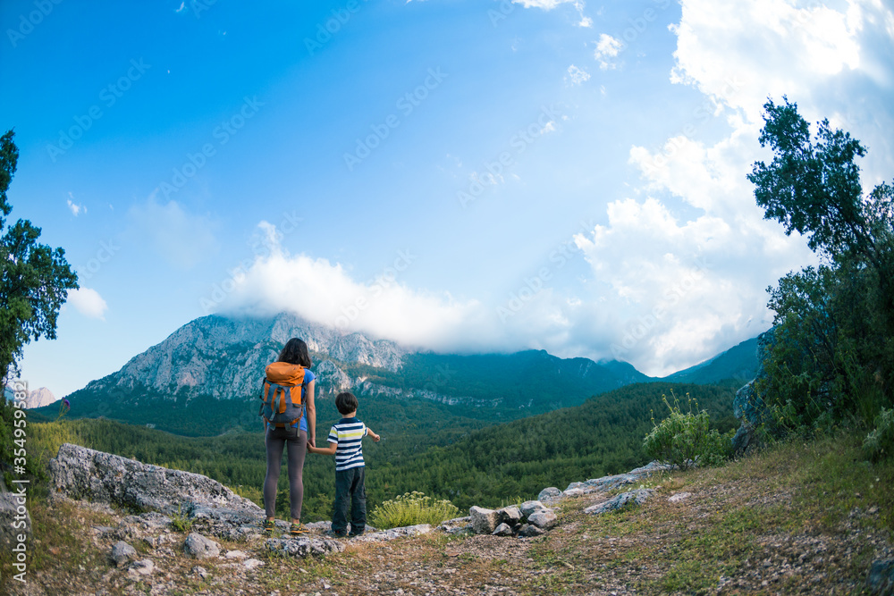 The boy and his mother are standing on the top of the mountain.