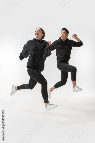 Running to freedom. Trendy fashionable couple isolated on white studio background. Stylish woman and man posing in basic minimal clothes equally suitable for both. Concept of equality, inclusive.