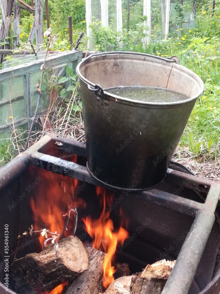 A bucket of water is heated on fire in a barrel on a garden plot. A bucket of water is heated on fire in a barrel on a garden plot.