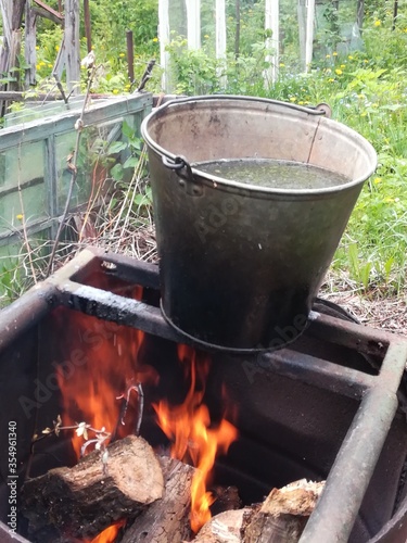 A bucket of water is heated on fire in a barrel on a garden plot.