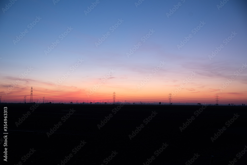 A landscape of a sunrise over a rural part of lower Austria with power lines, buildings, wind turbines in the background.