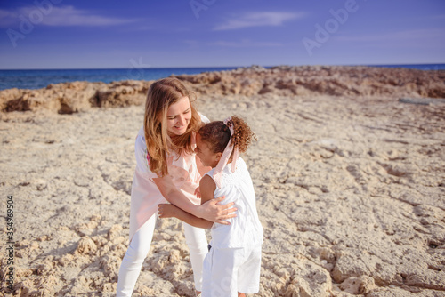Beautiful top view of young mother playing with daughter with white hat at the sea background. Family vacation. Travel. Female play with cheerful toddler. female with baby at ocean sunset.