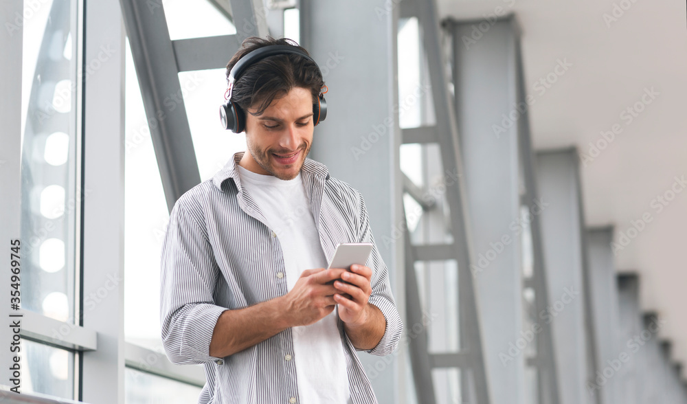 Travel Gadgets. Young Man With Wireless Headphones And Smartphone In Airport Travel Gadgets. Young Man With Wireless Headphones And Smartphone In Airport