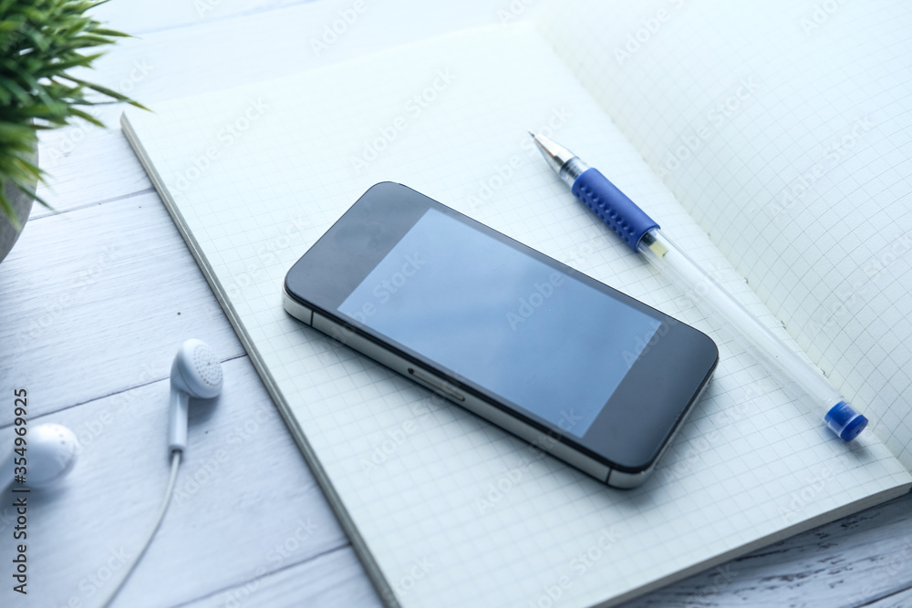 Close up of smart phone and pen on notepad on wooden table Close up of smart phone and pen on notepad on wooden table