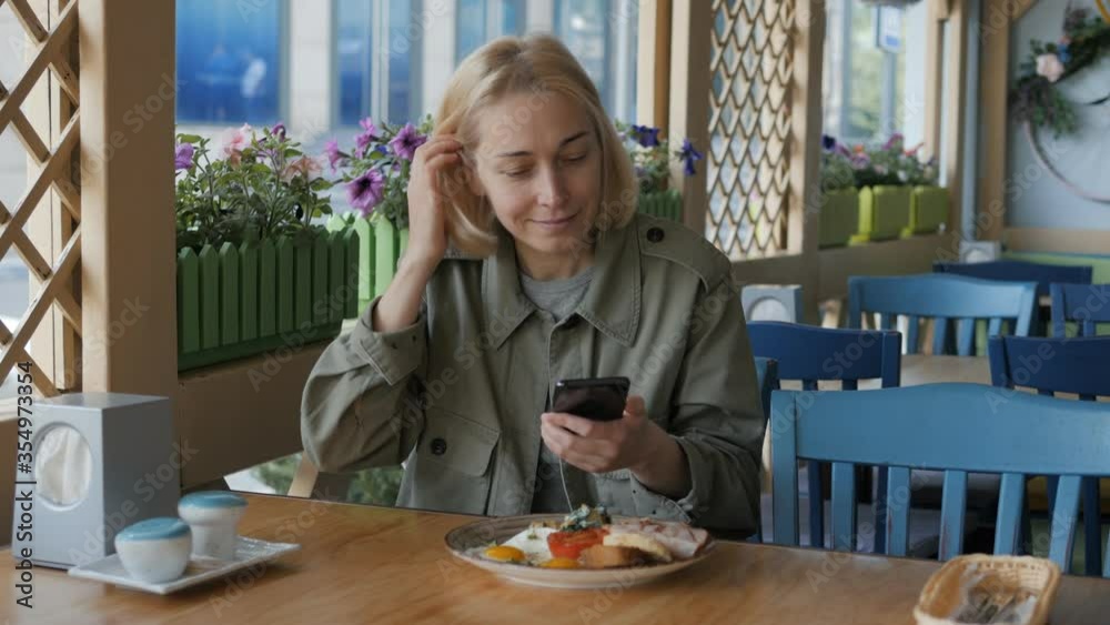 A woman using a smartphone camera takes a plate with Breakfast in a restaurant
