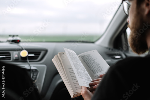 A man reads a book in a car during a long trip.