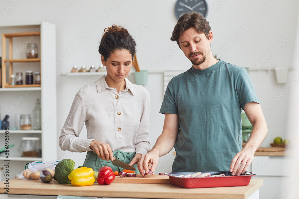 Young couple standing at the kitchen table and preparing dinner together in the kitchen at home Young couple standing at the kitchen table and preparing dinner together in the kitchen at home