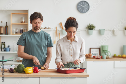 Young couple cutting vegetables at the table and preparing dinner together in the kitchen at home