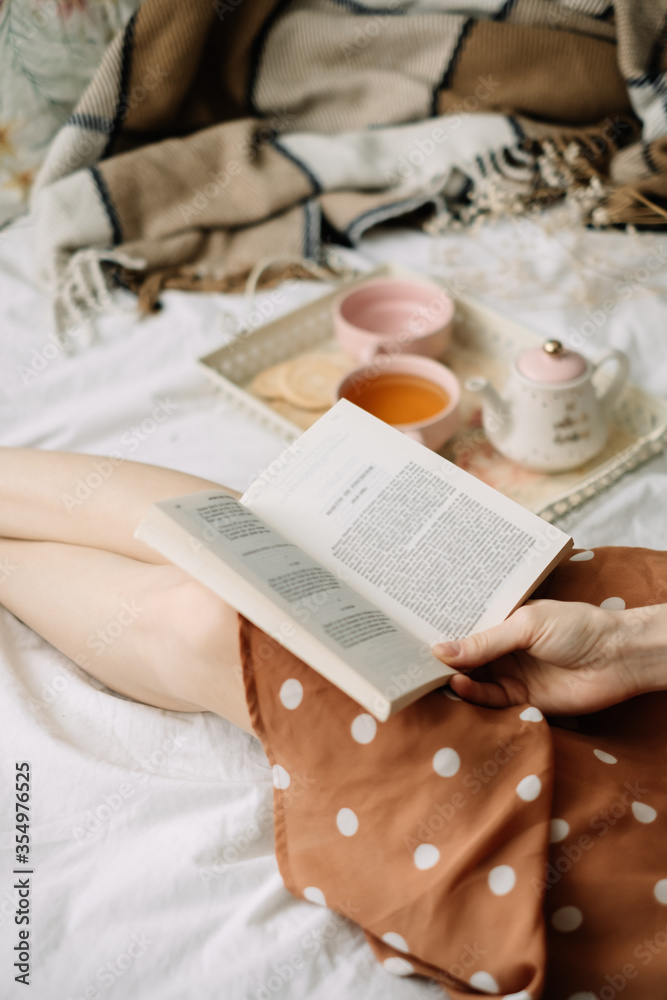 A woman reads a book at home in bed and drinks tea, home leisure in coziness and comfort.