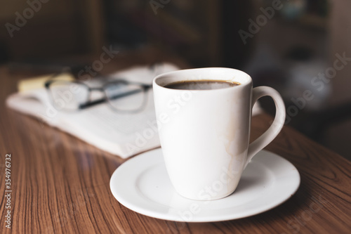 Cup of coffee with glasses and pen over book in background