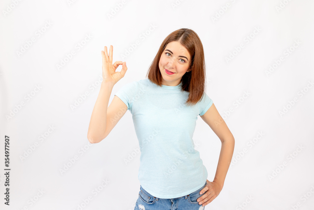 Portrait of a pretty brunette in jeans showing the OK sign and on a white background, space for text Portrait of a pretty brunette in jeans showing the OK sign and on a white background, space for text