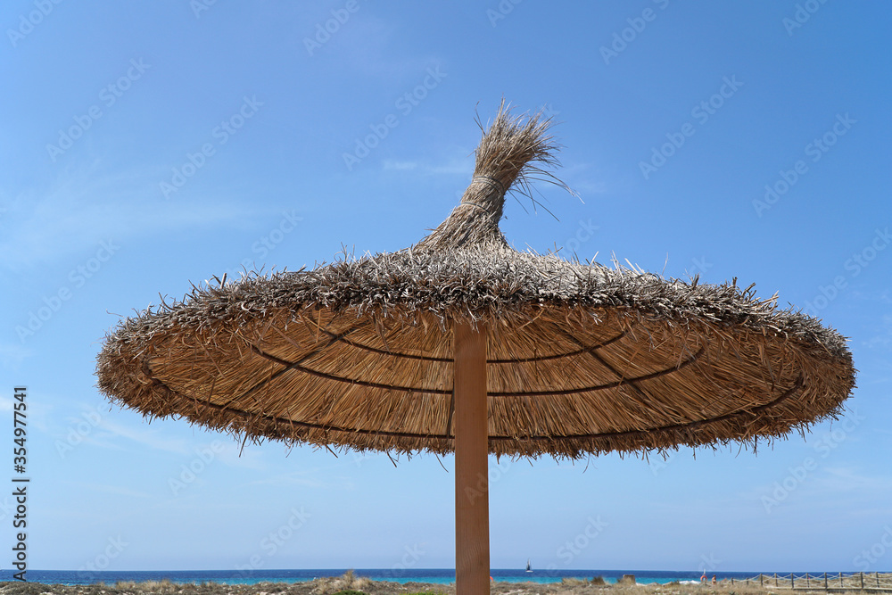 Palm tree leaf parasols against a blue summer sky and blue sea