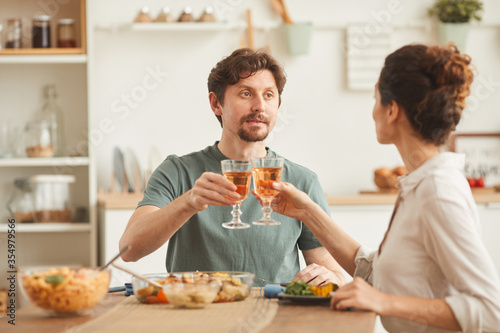 Young couple sitting at the table drinking wine and eating dinner in the domestic kitchen