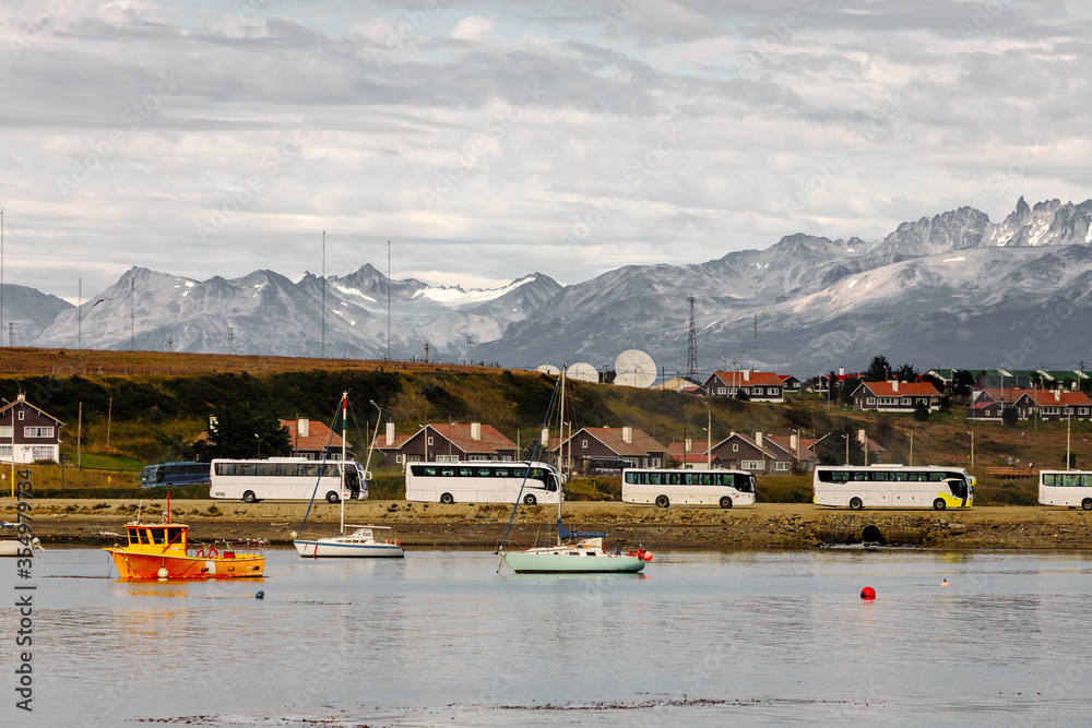 Row of bus charters parked in front of the port of Ushuaia (Argentina) with snowy mountains in the background