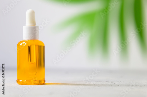 Dropper glass bottle oil mock up. osmetic pipette on gray background with tropical leaves shadows