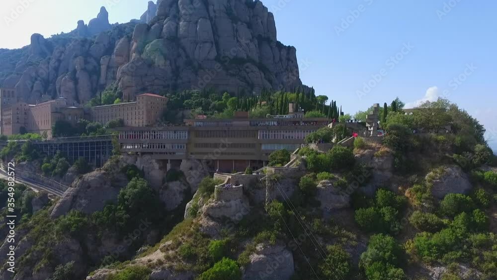 Aerial shot of tourists sitting on retaining wall at mountain, drone flying backward from people at famous landmark - Montserrat, Spain Aerial shot of tourists sitting on retaining wall at mountain, drone flying backward from people at famous landmark - Montserrat, Spain