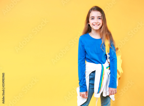 Caucasian child girl smiling face portrait with backpack on yellow background empty copy space.Teenager,teen age girl back to school concept.School child,schoolgirl.