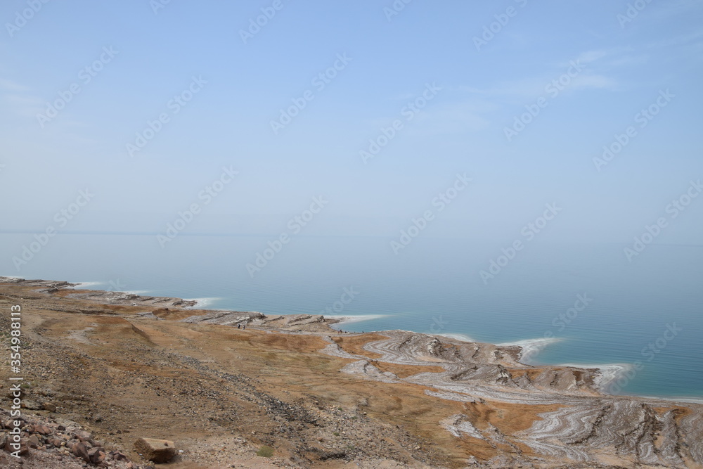 Dead Sea coast on the Jordanian side with salt deposits and bright blue water on a warm spring day, Dead Sea, Jordan