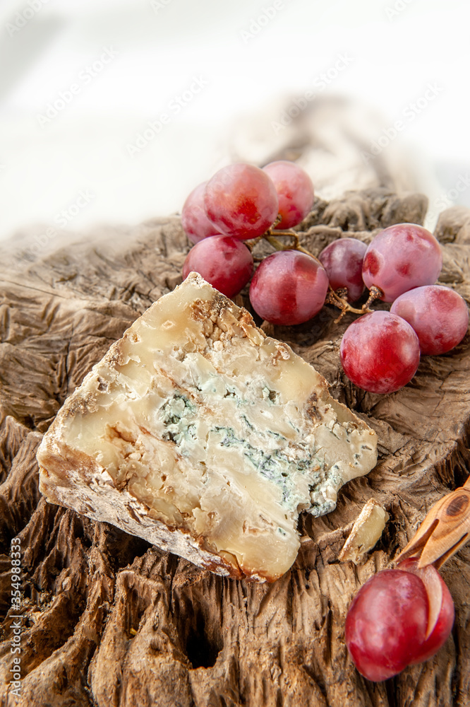 A piece of blue Stilton cheese on a wooden antique background with large red grapes. Close up
