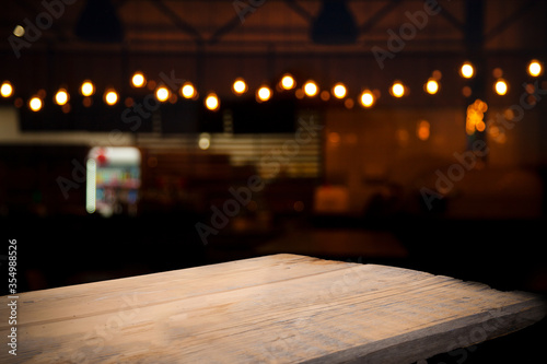 Empty wooden table top on blur light golden bokeh of cafe restaurant, bar in a dark background. © Egor