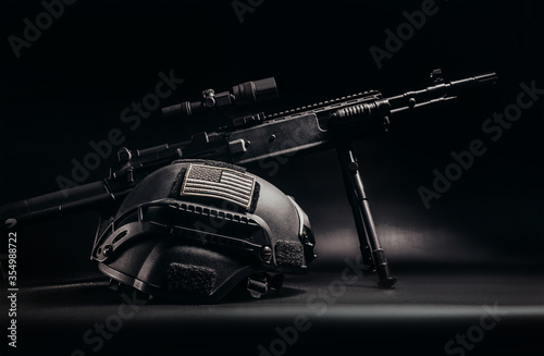 Foto Shaded sniper rifle with soldier helmet with american flag patch laying on table