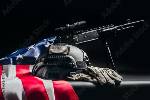 Sniper rifle with soldier armor helmet and american flag laying on table.