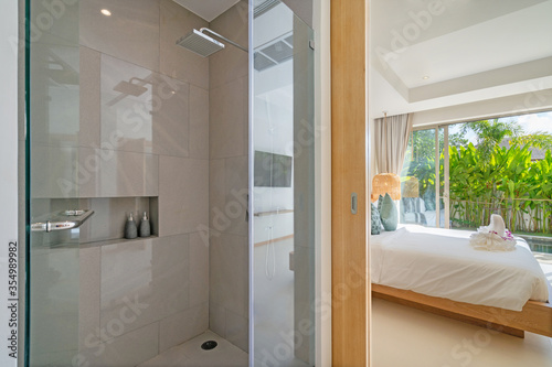 Interior design of shower room ensuite in bedroom in luxury villa feature shower head, sliding door joining to bedroom, bedding, towels on bed amd pool view photo