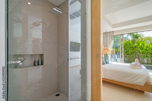 Interior design of shower room ensuite in bedroom in luxury villa feature shower head, sliding door joining to bedroom, bedding, towels on bed amd pool view