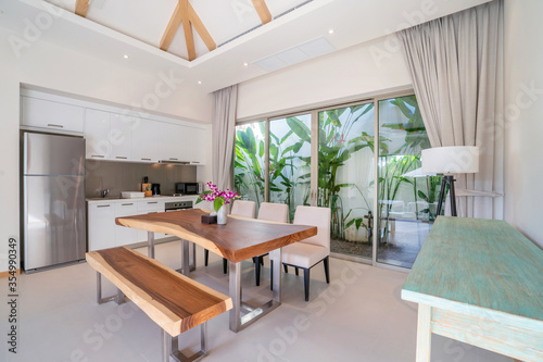 Interior design of kitchen in luxury villa, apartment feature wooden dining table, kitchen counter, refrigeratpr, oven, hood, microwave and sliding door to garden area