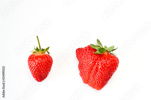 ugly strawberries and plain beautiful strawberries on a white background .Funny, unnormal fruits or food waste concept. Unformatted fruits