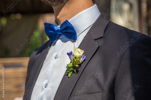  Groom at a wedding in a dark blue suit with a blue bow-tie and a rose in a buttonhole, shot close-up from a side angle.