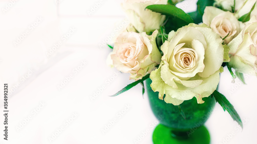 Romantic bouquet of delicate greenish roses in a green glass of thick glass on a light background. Close-up, copy space