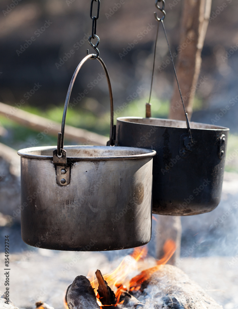 Cooking in two sooty old cauldrons on bonfire with smoke at forest Cooking in two sooty old cauldrons on bonfire with smoke at forest