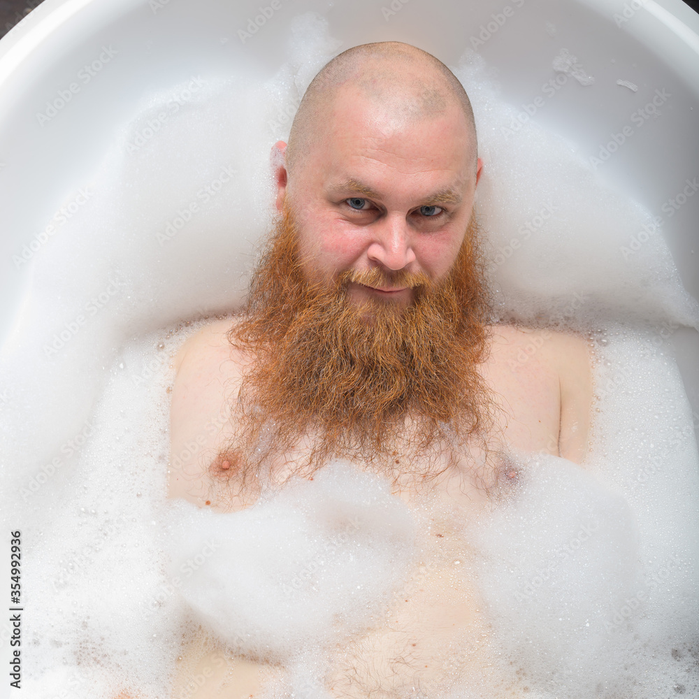 Portrait of a bald man fooling around in the foam bath. Top view on guy having fun in the bathroom. Portrait of a bald man fooling around in the foam bath. Top view on guy having fun in the bathroom.